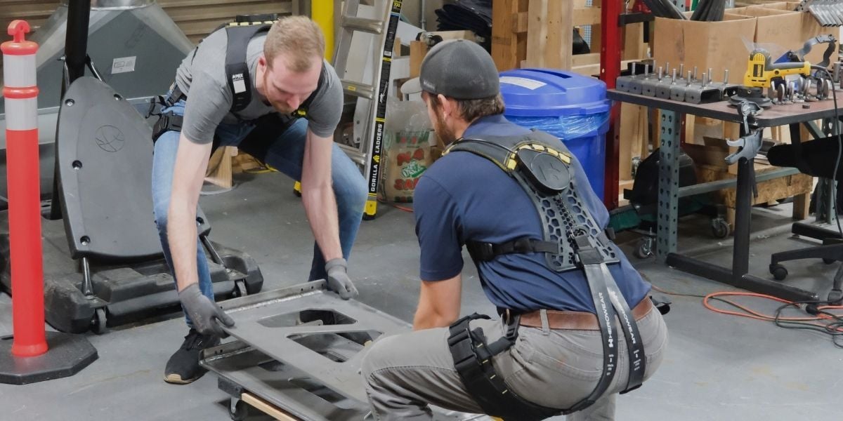 Two manufacturing workers wearing HeroWear Apex 2 exosuits while lifting heavy equipment